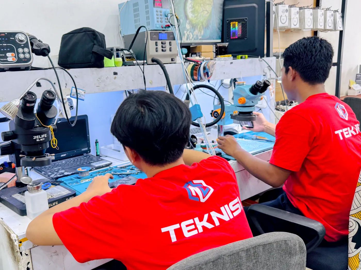 Teknisi NET CELLINDO Bekasi sedang memperbaiki HP dengan mikroskop & peralatan profesional